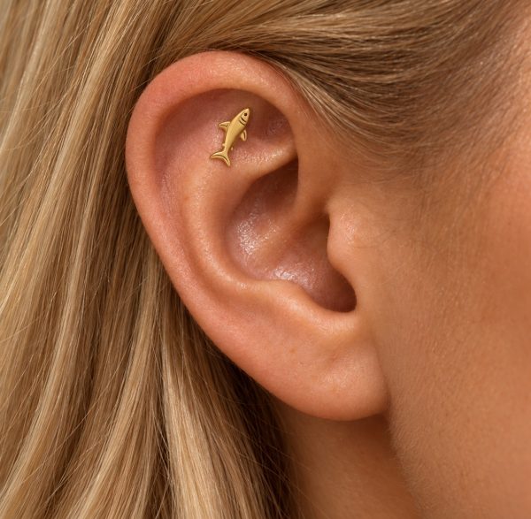 Small gold-tone shark stud positioned diagonally inside the upper ear of a long-haired woman