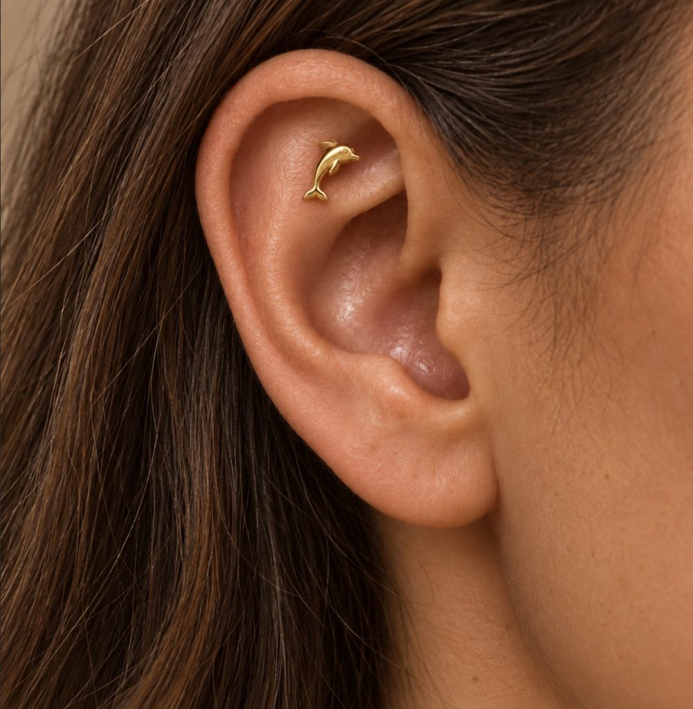 Small gold-tone dolphin stud nestled inside the upper ear of a woman with long brown hair