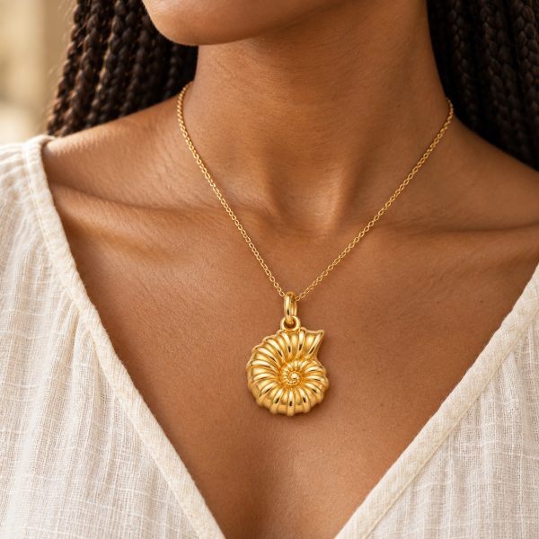 Woman wearing a gold-tone ammonite pendant on a fine matching chain with a cream blouse.