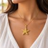 Woman wearing a gold-tone textured starfish pendant on a fine chain with an off-white blouse.