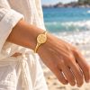 Gold-tone sand dollar open cuff bracelet with a five-petal centerpiece and smooth tapered band on a white background