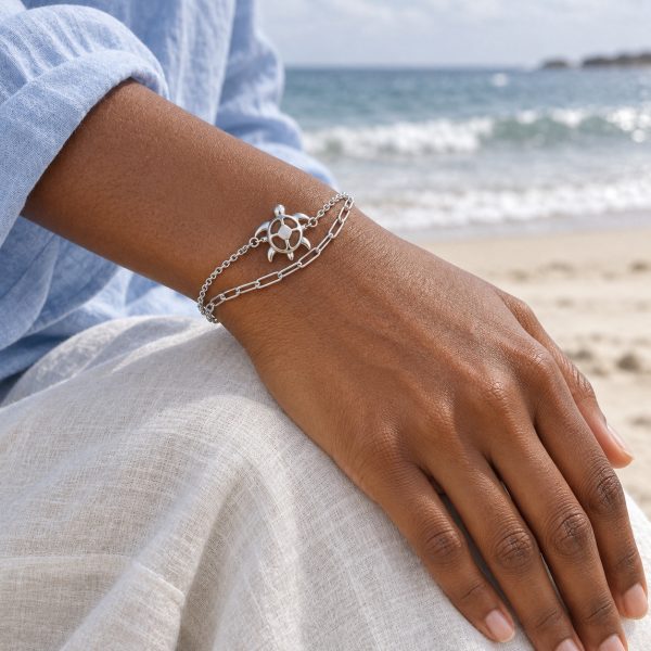 Silver-tone openwork sea turtle bracelet with cable and paperclip-style chains, lobster clasp and extension chain on white