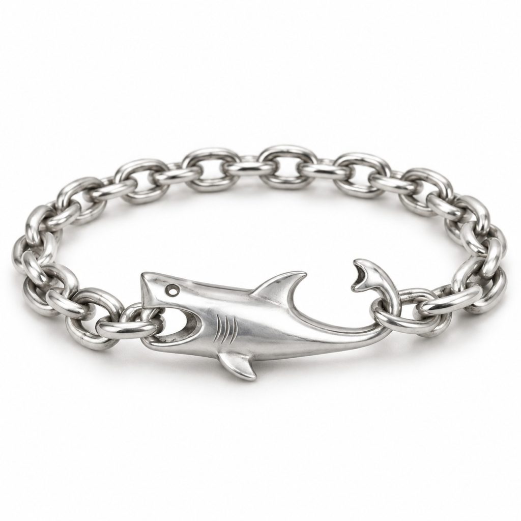 Silver-tone shark bracelet with a hollow eye, mouth holding a chain link and curved tail hook on a white background