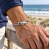 Silver-tone shark bracelet with a hollow eye, mouth holding a chain link and curved tail hook on a white background