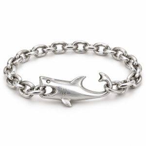 Silver-tone shark bracelet with a hollow eye, mouth holding a chain link and curved tail hook on a white background