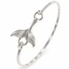 Silver-tone whale tail bangle with sculpted flukes, a slim oval band and hook-and-ring connections on white
