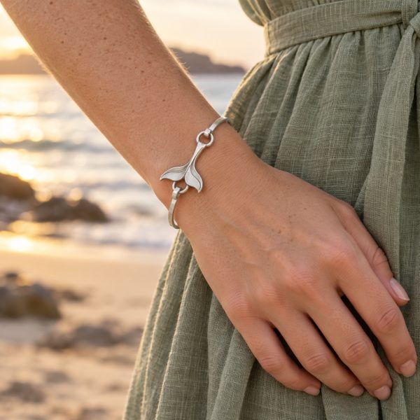 Silver-tone whale tail bangle with sculpted flukes, a slim oval band and hook-and-ring connections on white