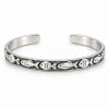 Silver-tone fish pattern cuff bracelet worn on a woman's wrist beside driftwood at the beach