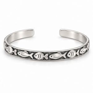 Silver-tone fish pattern cuff bracelet worn on a woman's wrist beside driftwood at the beach
