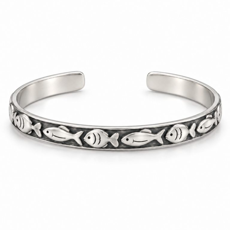 Silver-tone fish pattern cuff bracelet worn on a woman's wrist beside driftwood at the beach