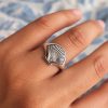 Silver-tone scallop shell signet ring worn on a finger, showing its fan-shaped face and ribbed texture