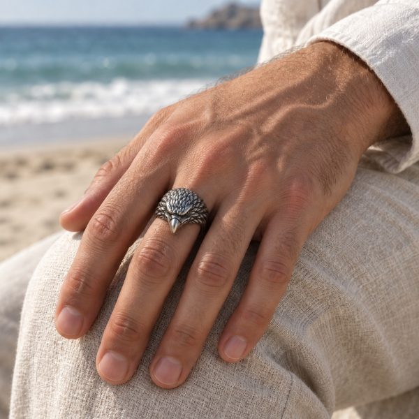 Silver-tone eagle head ring worn on a finger, showing its curved beak and sculpted feather details